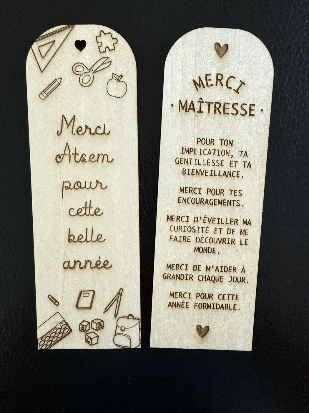 Gros plan sur deux marque-pages en bois gravés « Merci Maîtresse » et « Merci ATSEM »