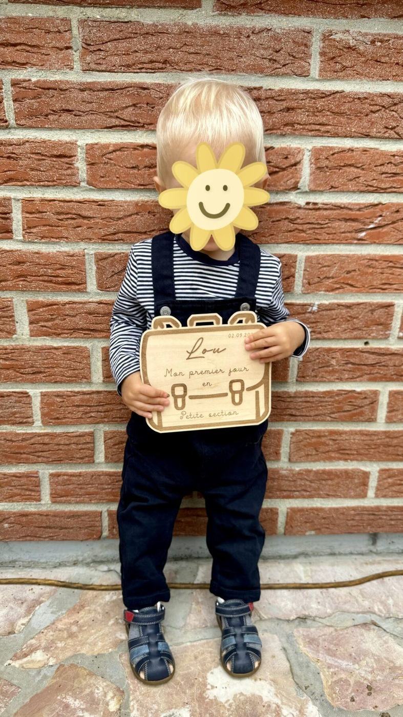 Enfant tenant sa plaque premier jour d'école devant un mur de briques